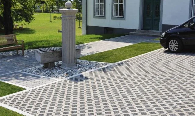 Acceso residencial con piezas de concreto perforadas y césped entre sus aberturas, junto a una vivienda.
